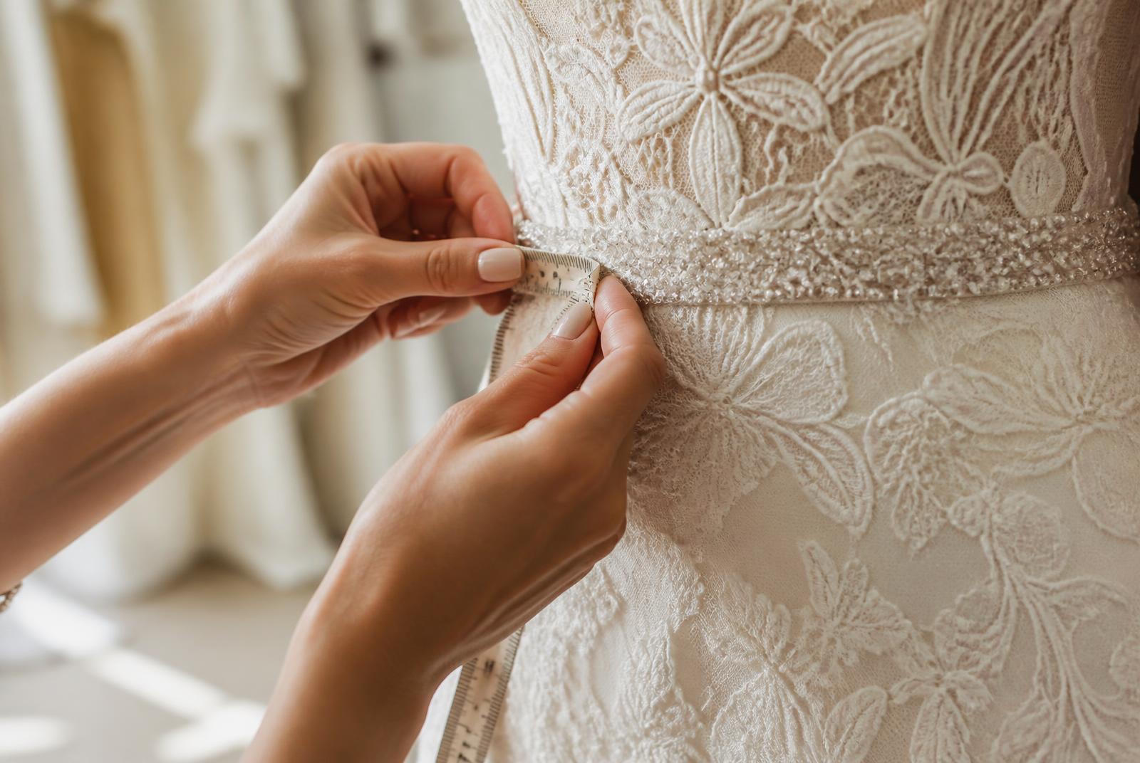 Measuring the beaded waistband of a lace wedding dress during a wedding dress alteration fitting
