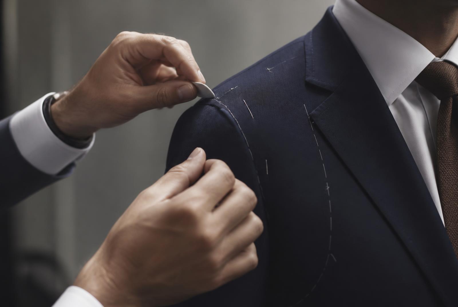Tailor pinning the shoulder of a navy suit jacket during a gentlemen's suit alteration fitting