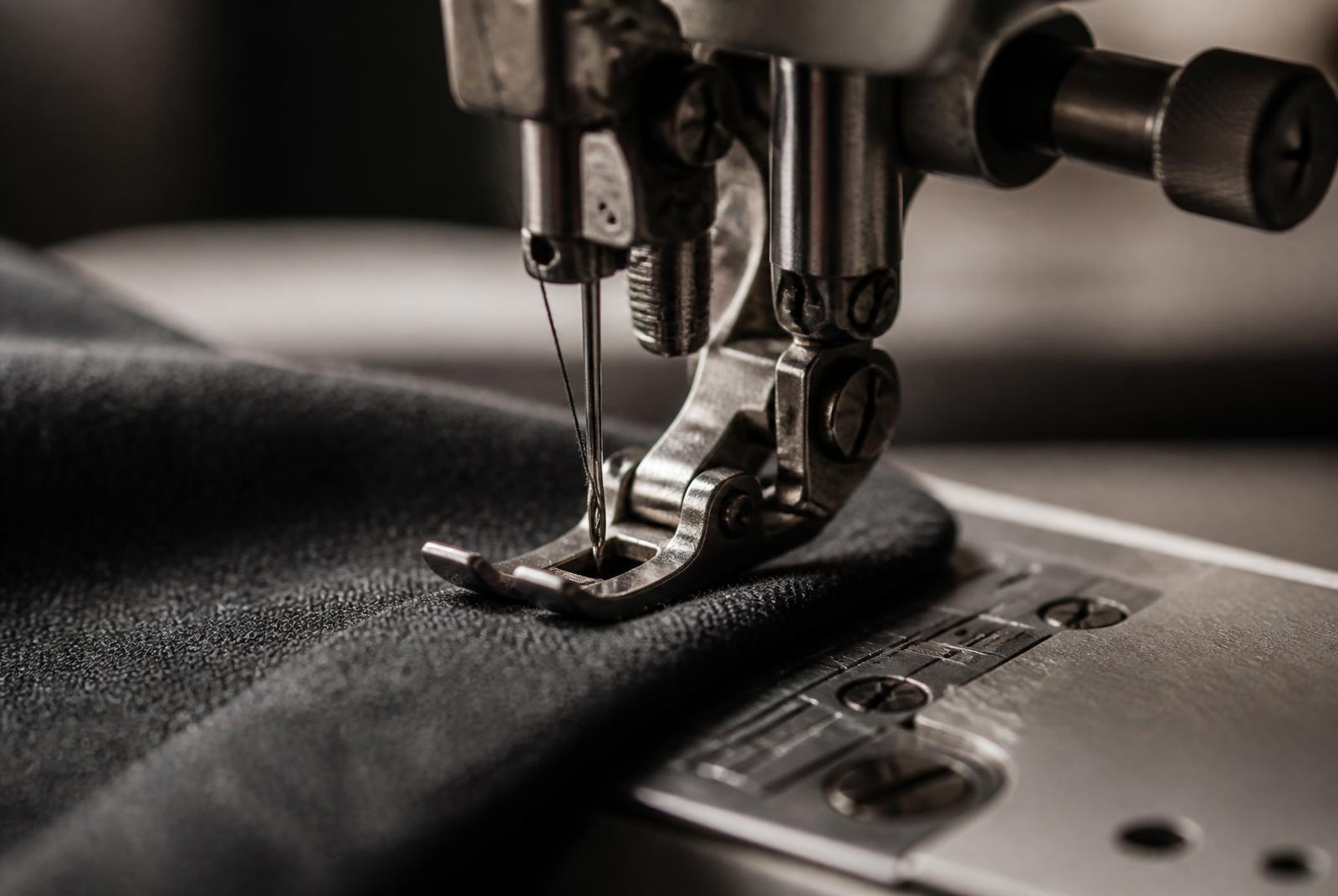 Close-up of a fine charcoal wool hem being stitched on an atelier sewing machine